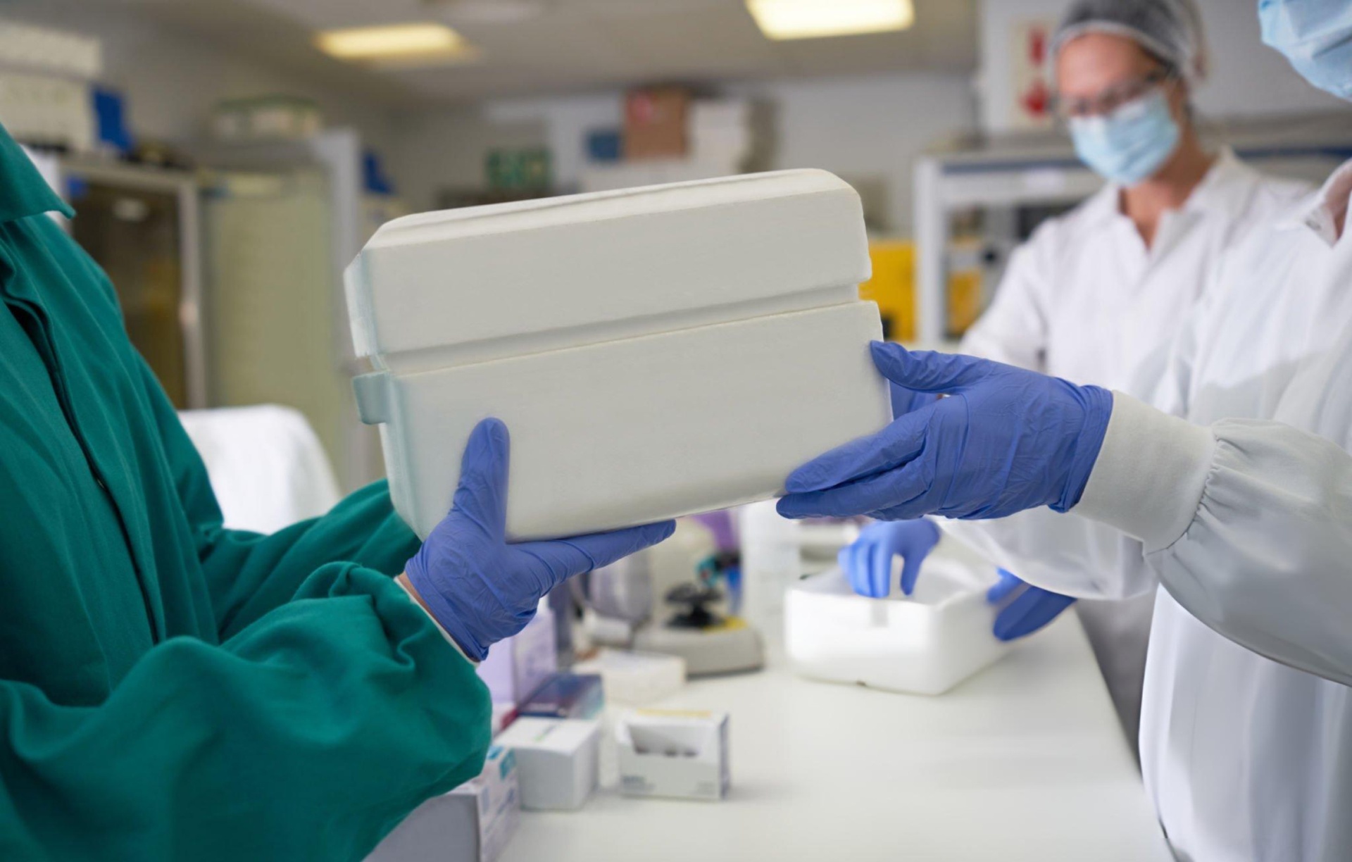 Clinical handoff of a temperature-controlled specimen cooler between gloved hands in a laboratory