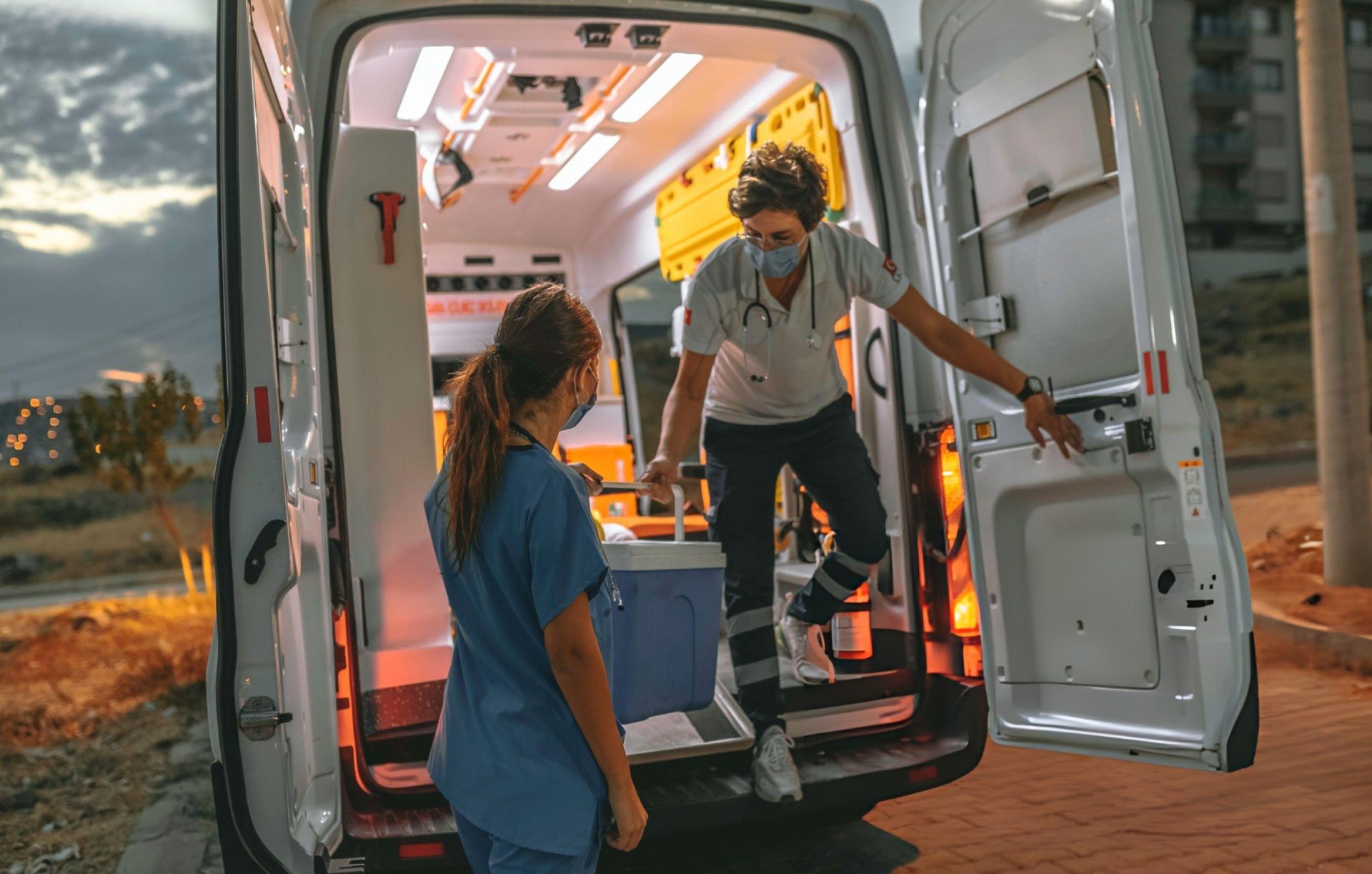 Medical team transferring a transport cooler from an ambulance at dusk